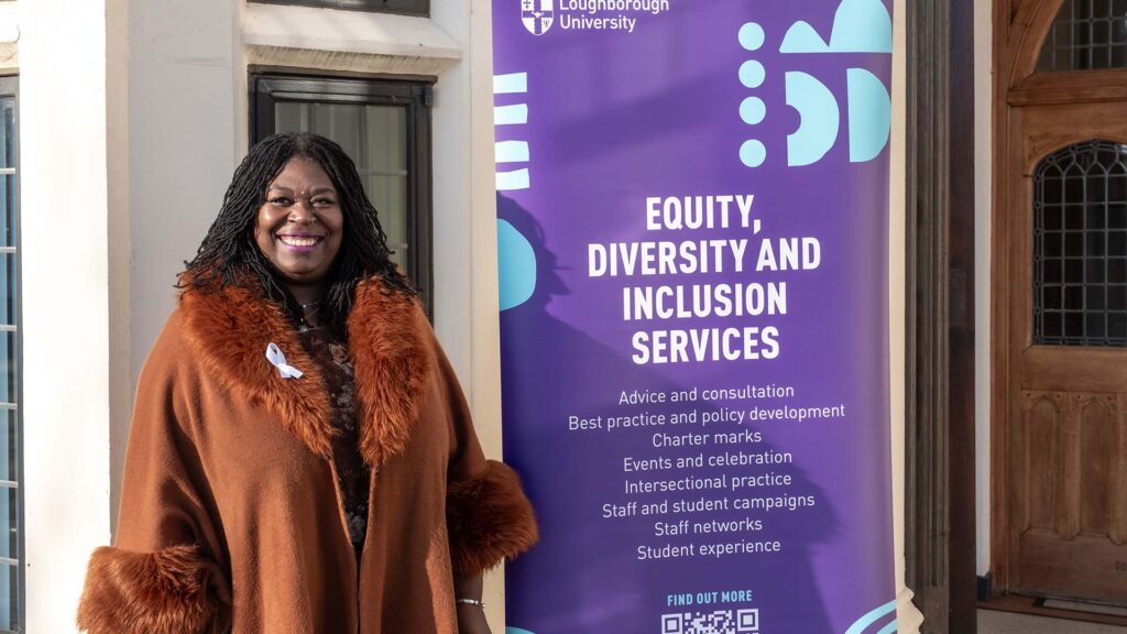 Veronica stood outside a building next to a pull up banner with information about the Equity Diversity and Inclusion Services team. 