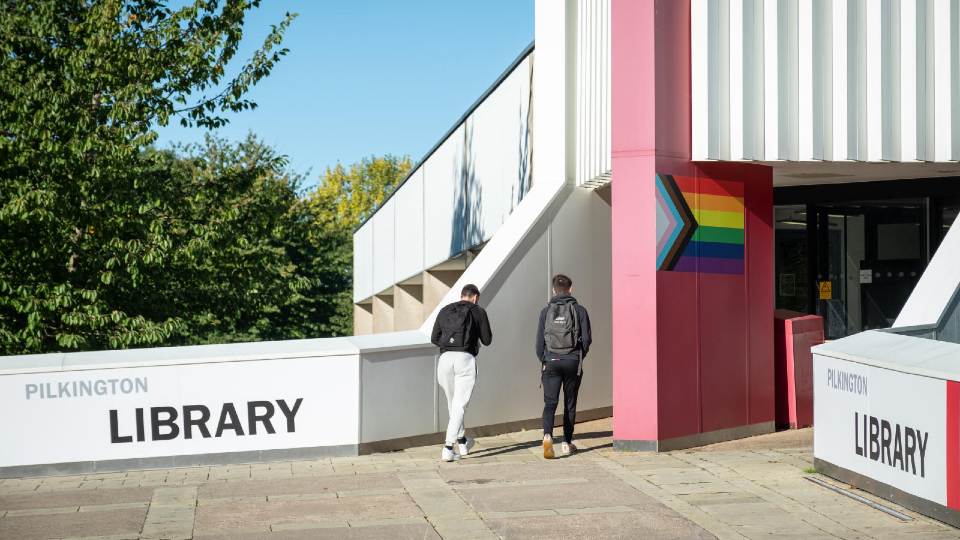 Two students walking into the entrance of Pilkington Library