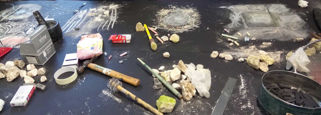 A range of drawing instruments including chalkstones, string, and brushes laid out on a black floor.