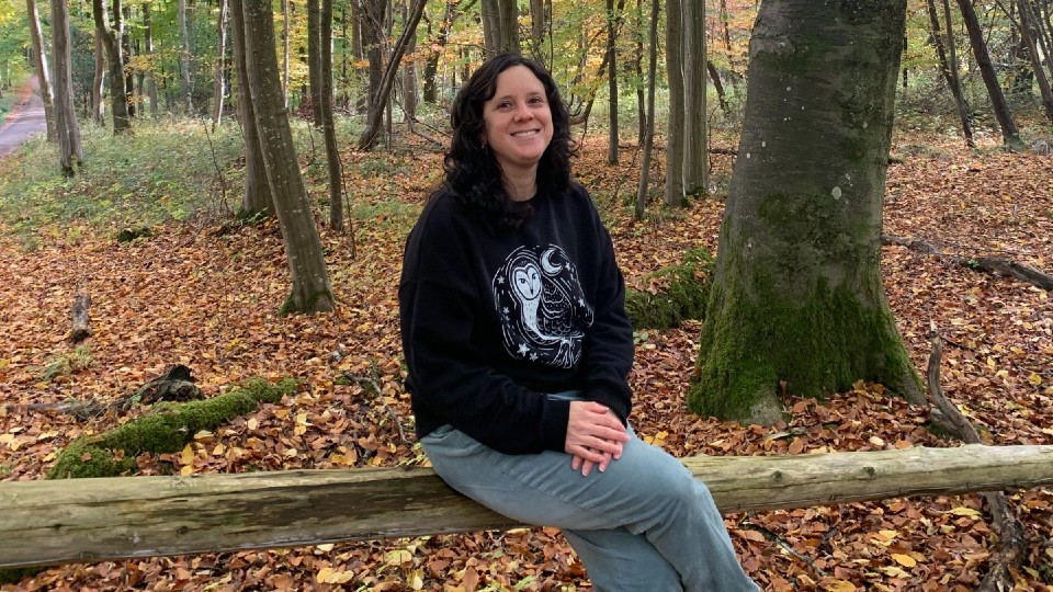 Lucrecia Alvarez-Barrantes sitting on a log in a woodland area.