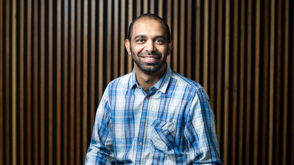 Close-up of Yasir Ali in front of a wooden background.