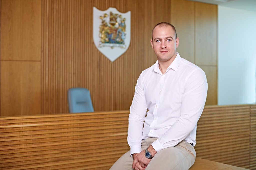 Dom Willmott sitting on a wooden bench in a court room.