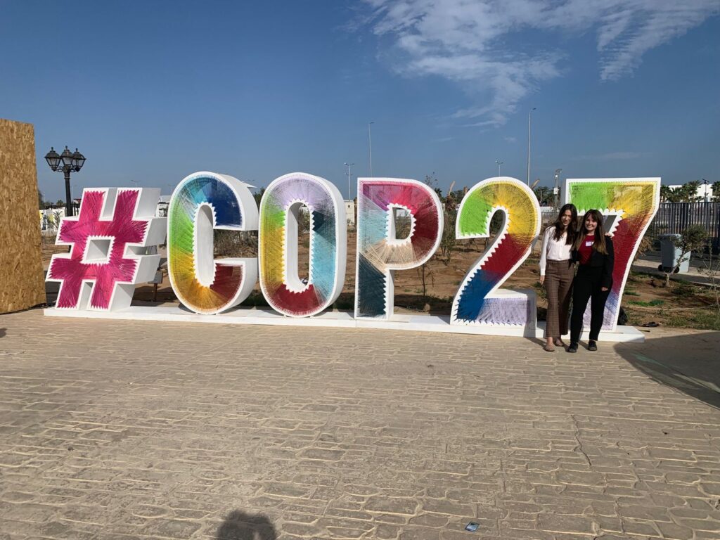 Erin and a friend in front of big letters saying 'COP27'