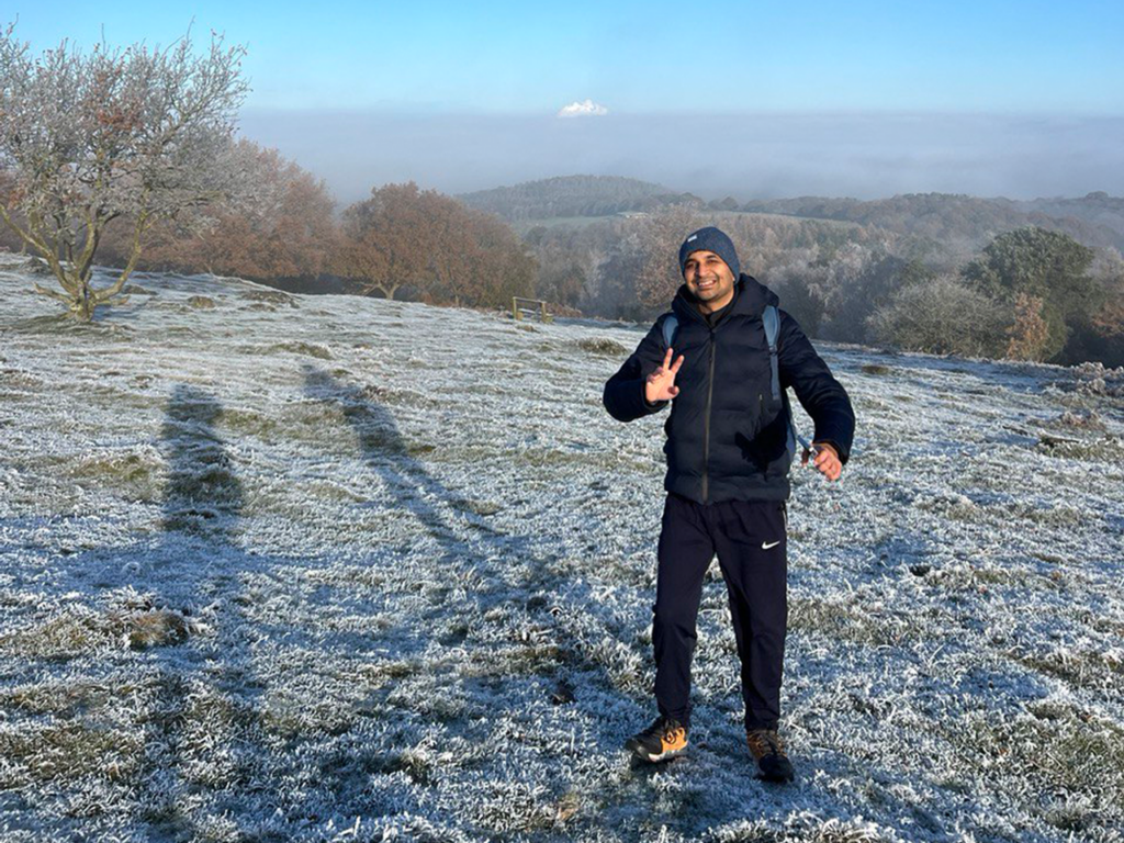Mehul smiling and making a peace sign on top of a frosty hill