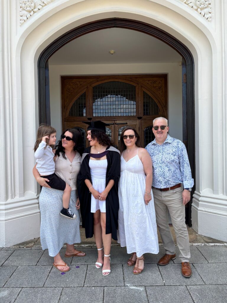 Lauryn in a cpa and gown in the middle of 3 adults and a child in front of the Rutland Building