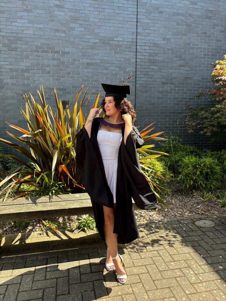 Lauryn in a cap and gown in front of a plant