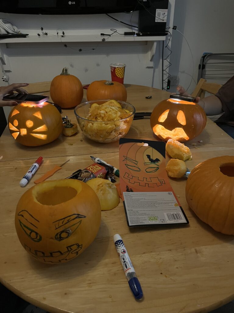 6 pumpkins on an oval table being carved. 2 are finished with lights in