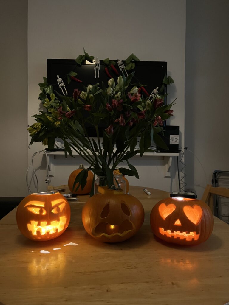 3 carved pumpkins with lights in in front of a bunch of flowers