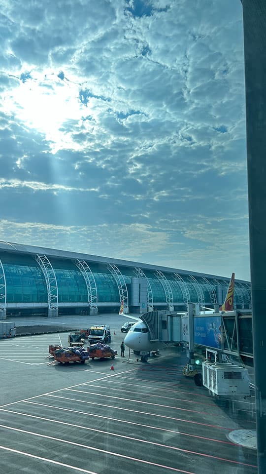 An aeroplane and passenger boarding bridge, seen from an airport window on a bright but cloudy day