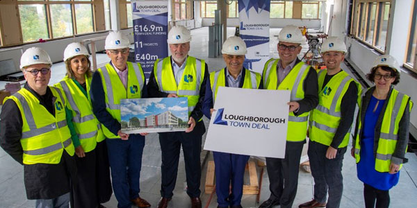 Eight people standing in a row wearing hard hats and hi-vis jackets holding a sign saying 'Loughborough Town Deal'
