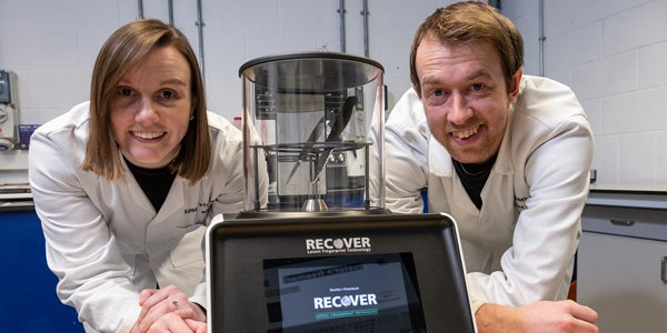A man and woman wearing white lab coats pose in front of the 'Recover' device.