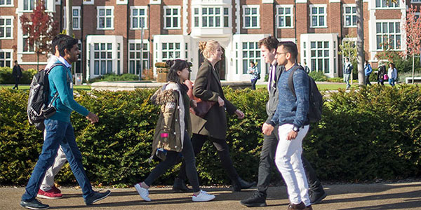 Six students walking in front of a hedge. The Rutland building is in the background.