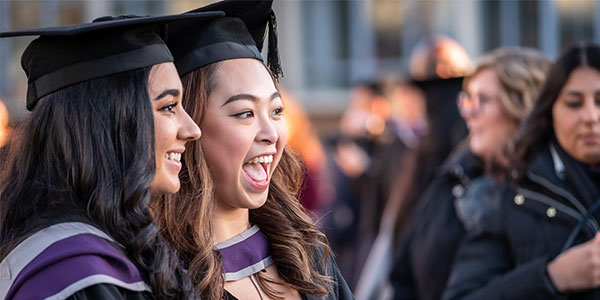 Two female students in graduation robes and hats posing for a photograph