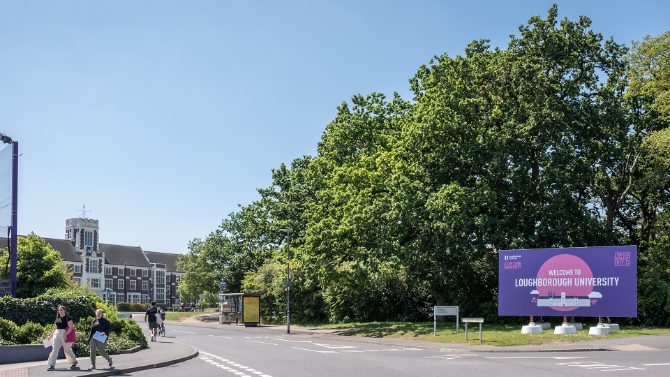A clear day on Loughborough  University campus, the 'Welcome to Loughborough University' sign and Hazlerigg Building in the background.