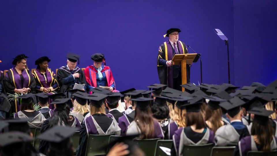 Vice-Chancellor Professor Nick Jennings wearing graduation wear, standing on stage at a December 2023 graduation ceremony, talking to a group of graduates sitting in the audience.