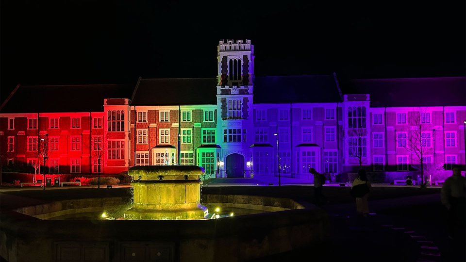 Hazlerigg building and fountain lit up at night by rainbow coloured lights.