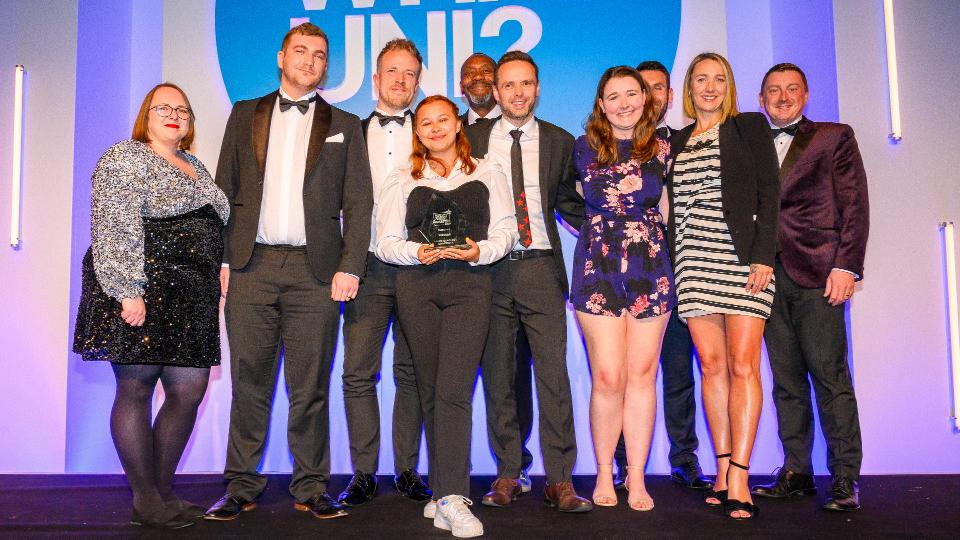 A group of staff from Loughborough stood on the stage holding an award and smiling at the camera.