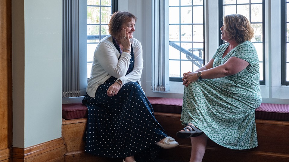Two people sat by a window having a conversation.