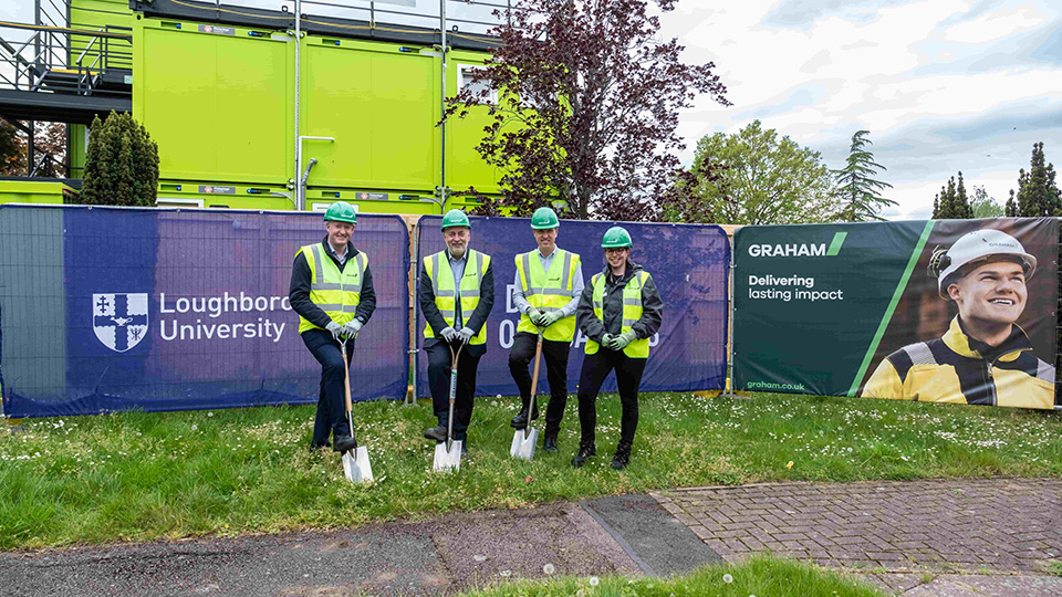 Four members of staff including Professor Nick Jennings wearing hi-vis jackets and green helmets standing outside of the new student accommodation development on campus.