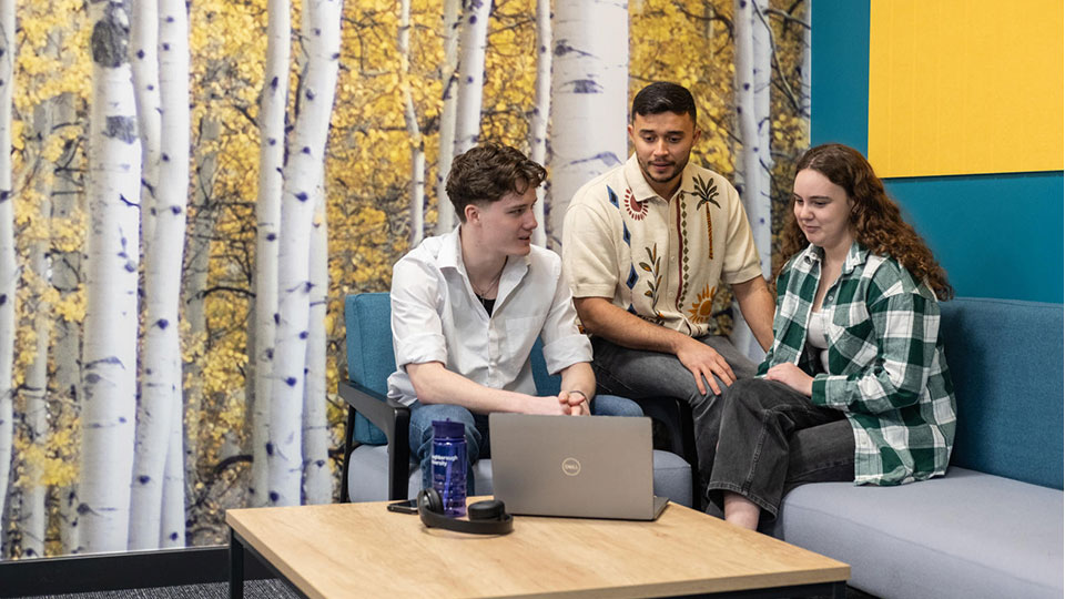 Three students on campus talking to each other in front of a laptop